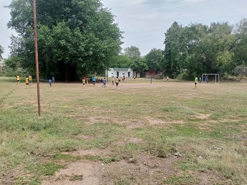 Wide view of the patchy grass ground with trees and school buildings behind