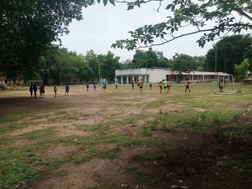 Bare, uneven ground with scattered students in the distance